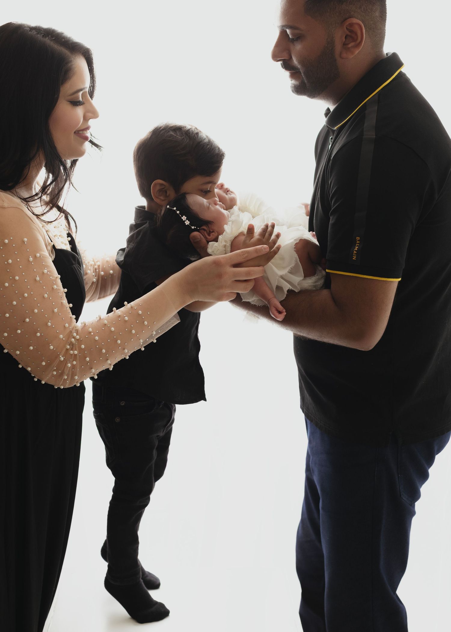 Elizabeth Lang Photography newborn photos mom and dad hold newborn twin girls in a bright backlit photo with little white dresses. brother