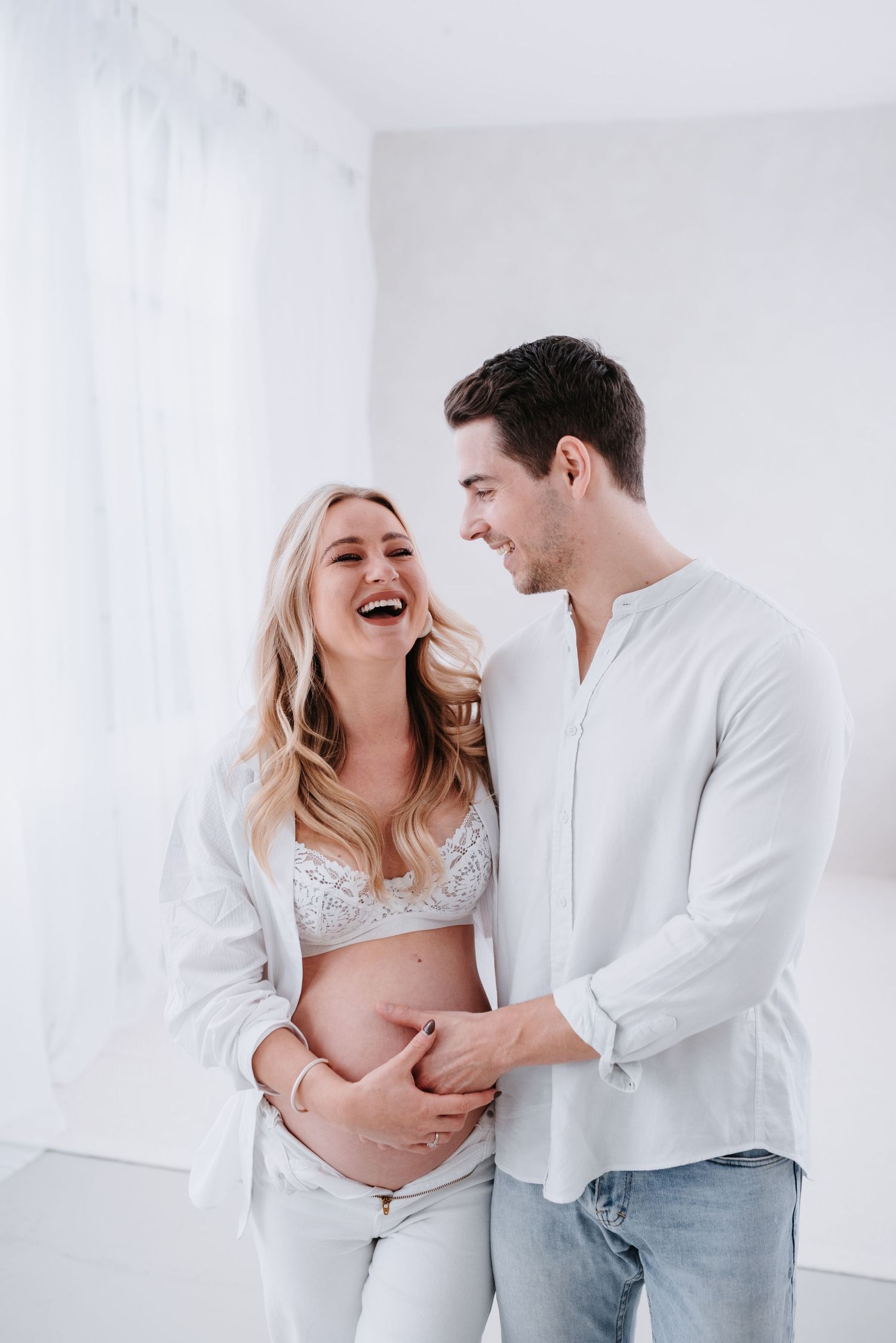 A joyful maternity photoshoot capturing intimate moments between an expecting couple in a bright white studio setting.