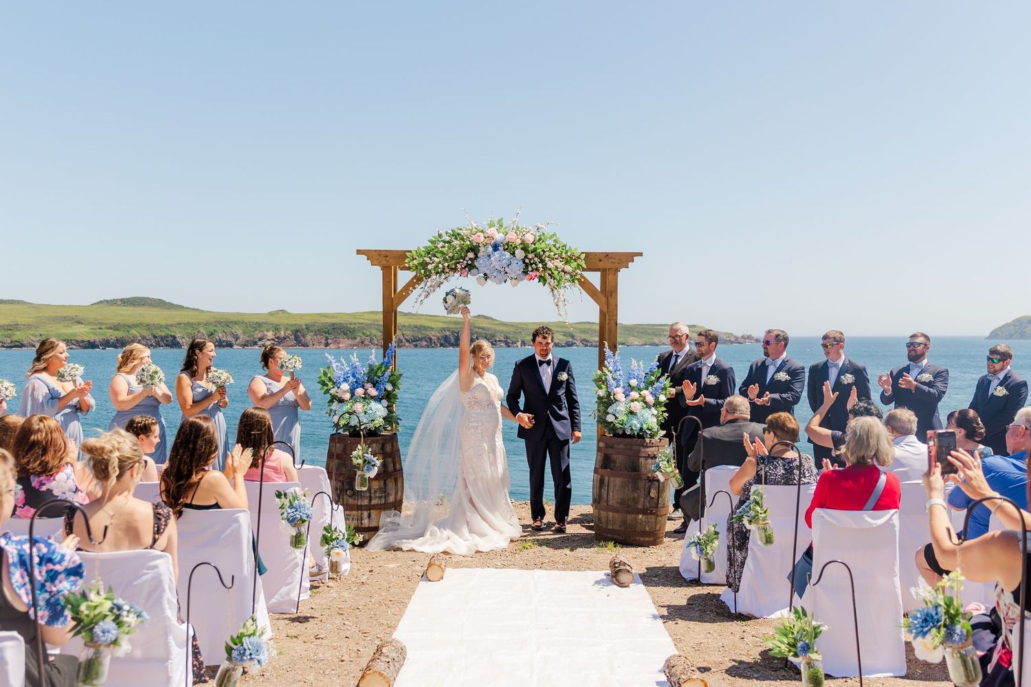 Outdoor wedding ceremony setup on a hillside with wooden arch and white chairs overlooking a scenic blue lake.