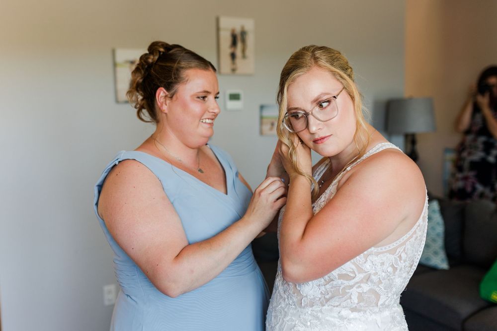 Someone helps with final wedding dress preparations in a serene, sunlit room.