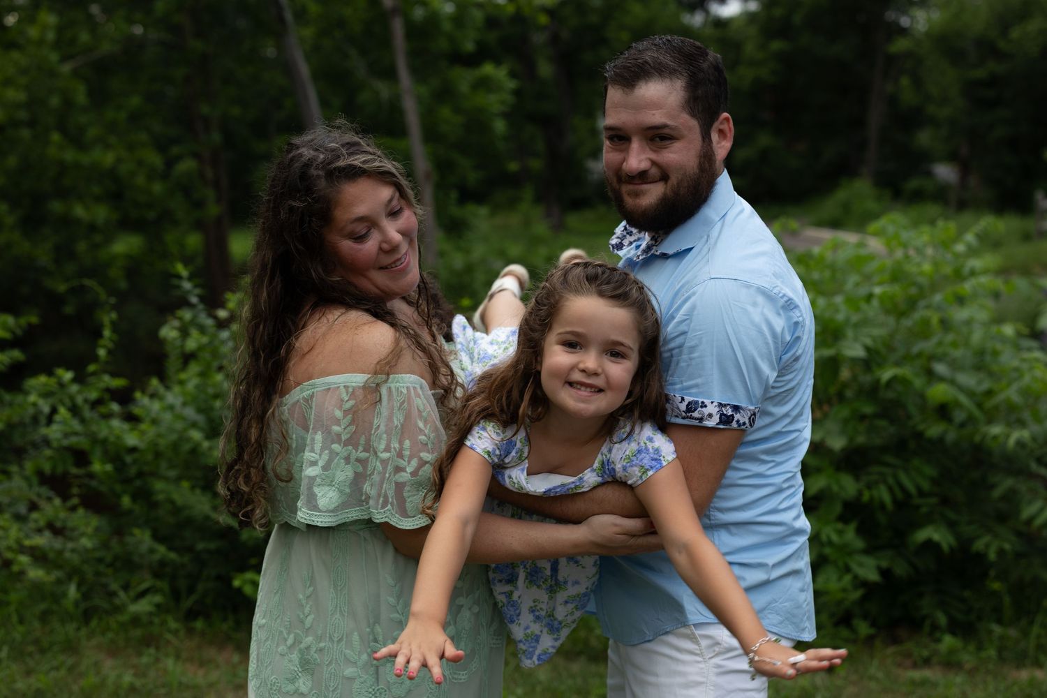 A family poses together outdoors against a natural green backdrop with trees and foliage.