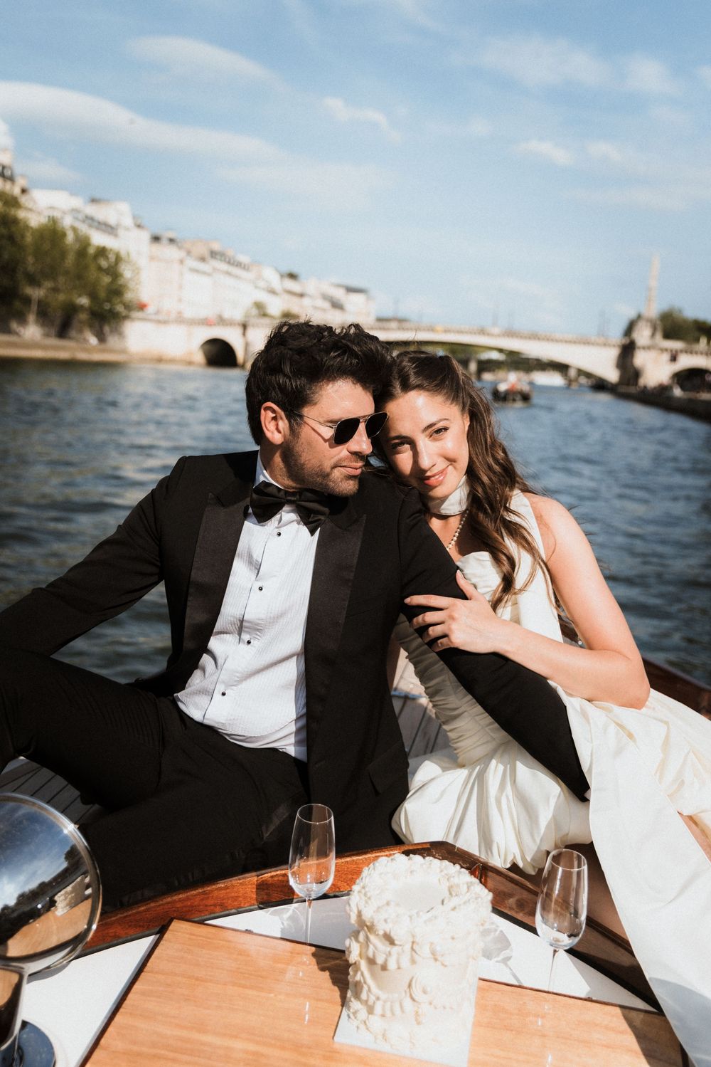 Couple sharing romantic moments and cake on a boat in Paris with scenic river views in the background.