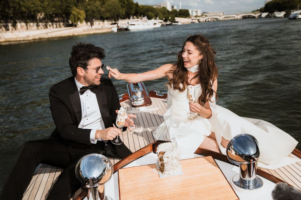 Couple enjoying drinks and laughter during a boat ride along a scenic European waterway.