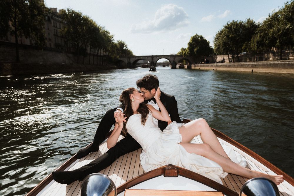 Wedding couple lounges on a wooden boat while cruising down a scenic river.