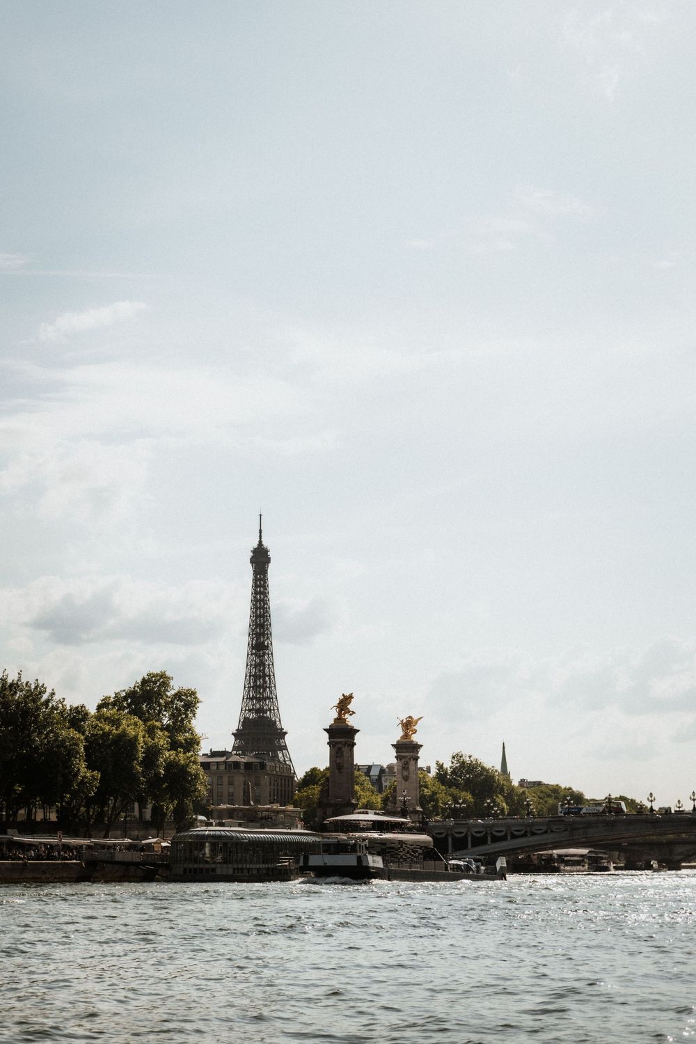 Three views of the iconic Eiffel Tower photographed from the Seine River in Paris with boats and bridges visible in the distance.