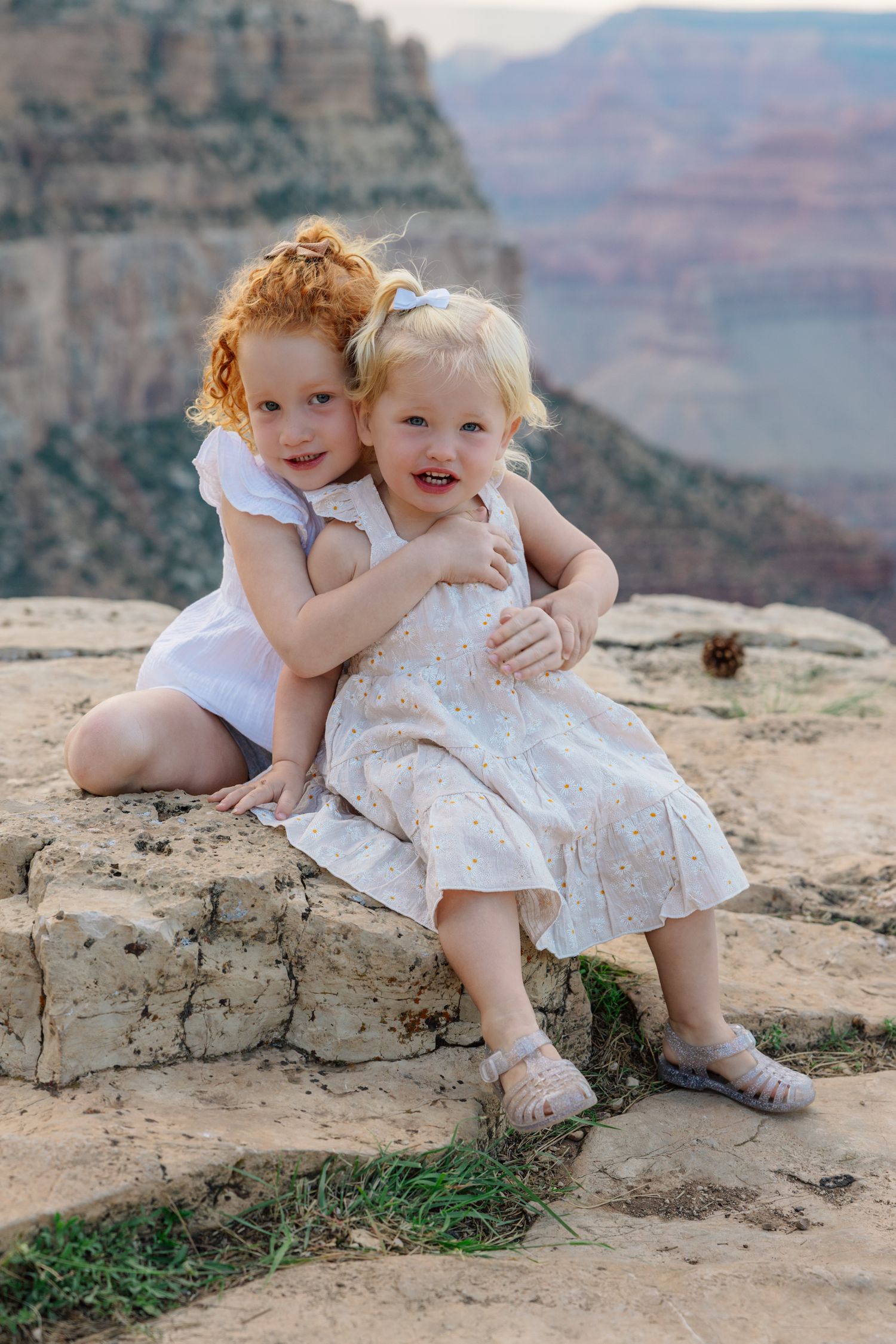 Two children sitting together and embracing at the edge of the Grand Canyon with dramatic cliffs in the background.