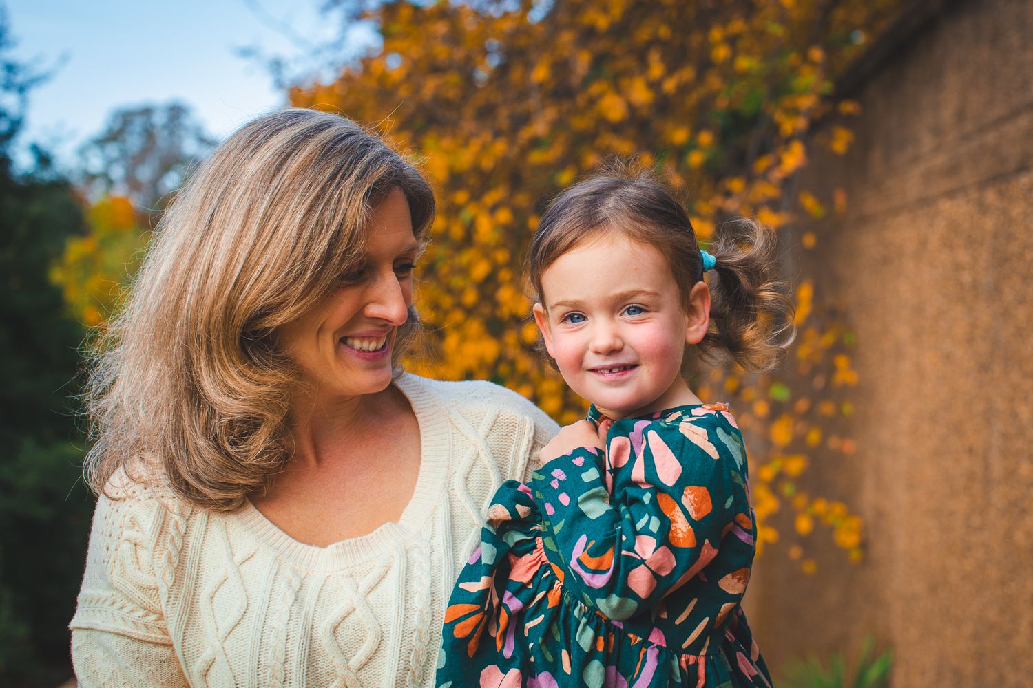Candid autumn portrait of mother and daughter against fall foliage.