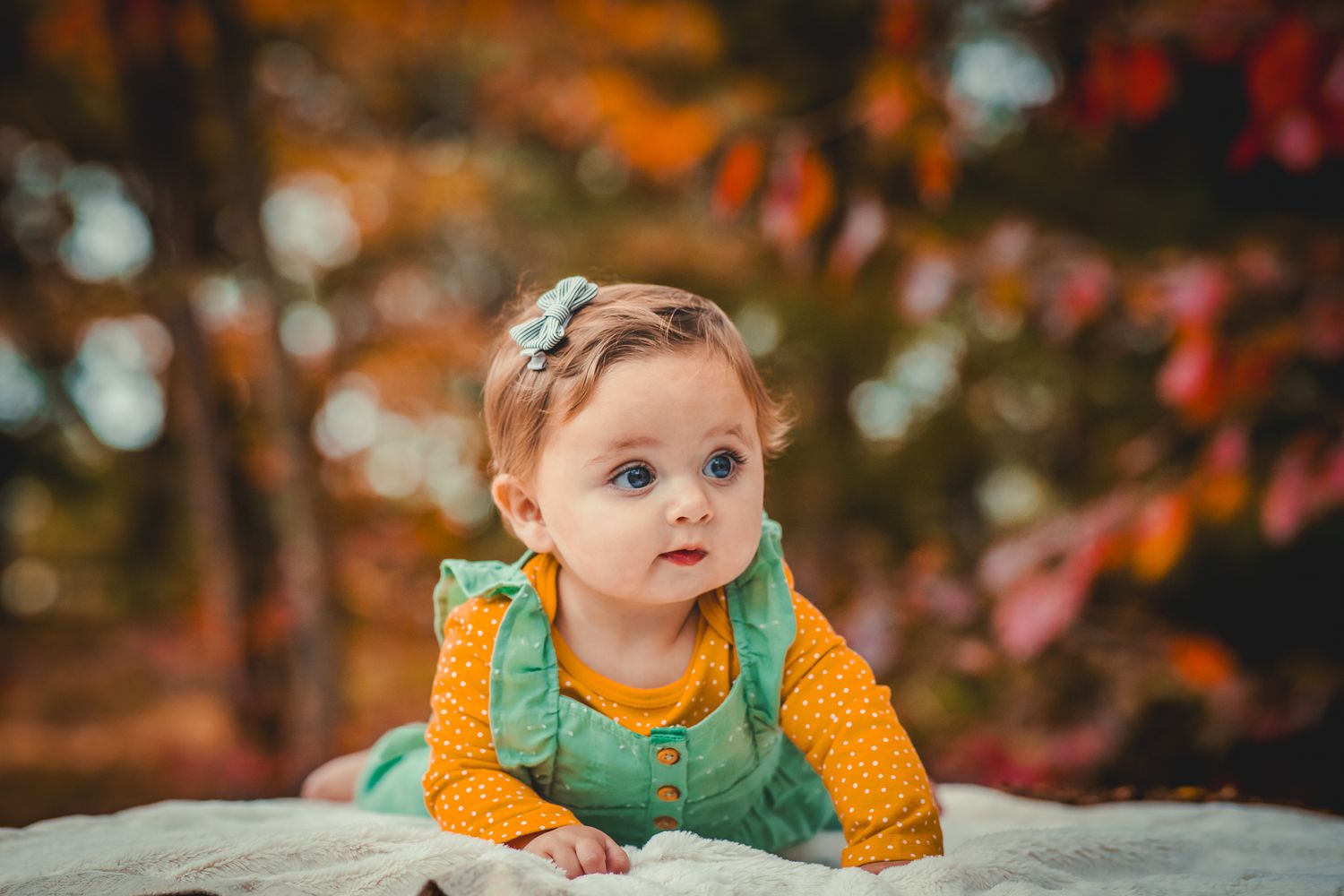 Baby in orange and green outfit lying on stone during autumn.