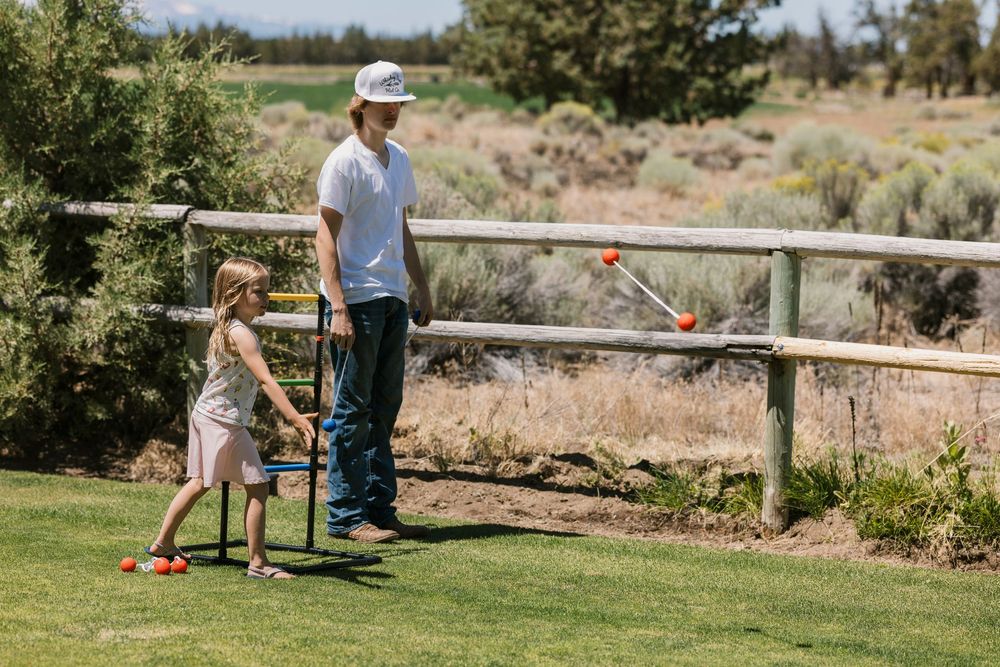 A parent and child spending time together playing croquet on a sunny lawn near a rustic wooden fence.
