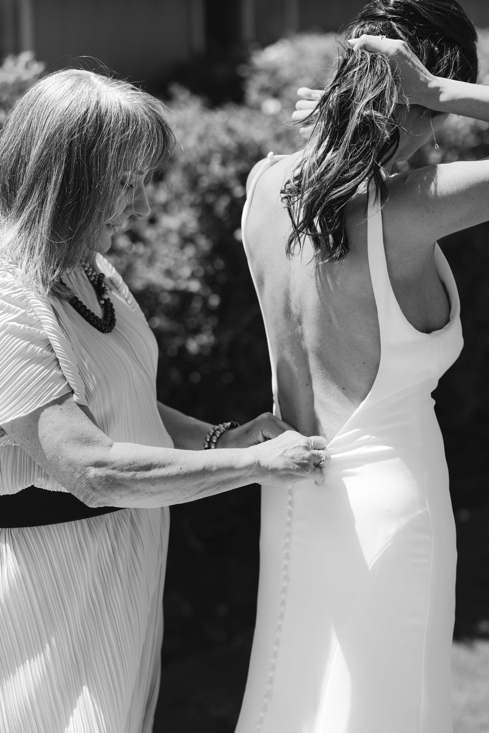 Black and white photo showing final adjustments being made to a classic white wedding dress.