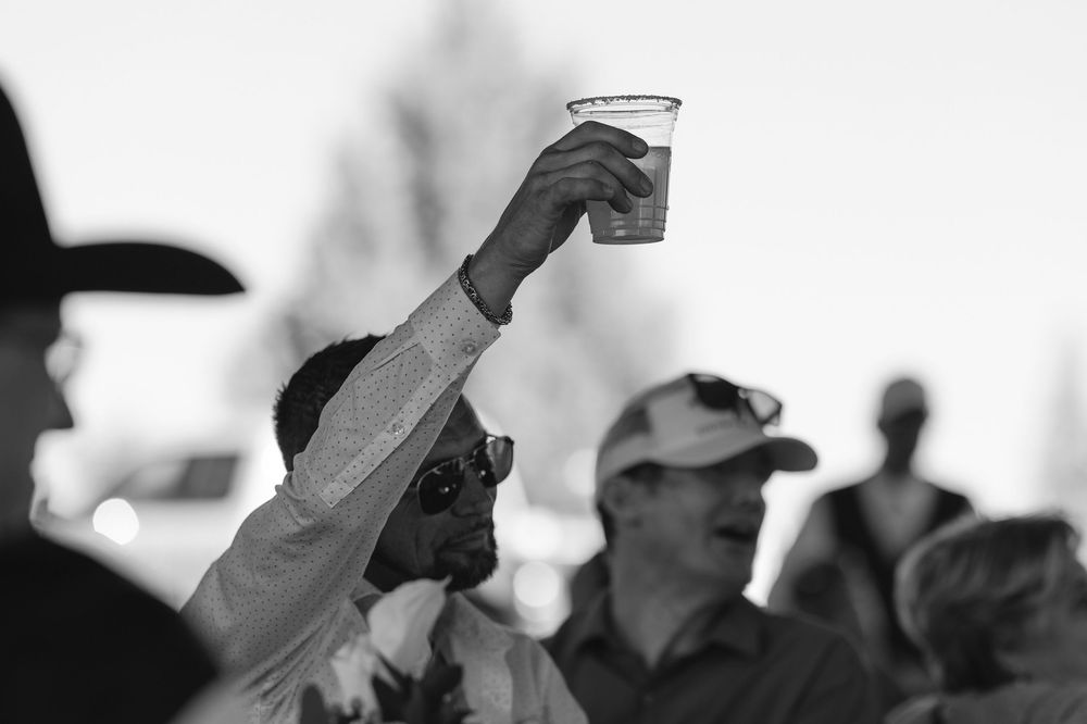 Black and white photo of someone raising a glass in a toast amidst a crowd at an outdoor gathering.