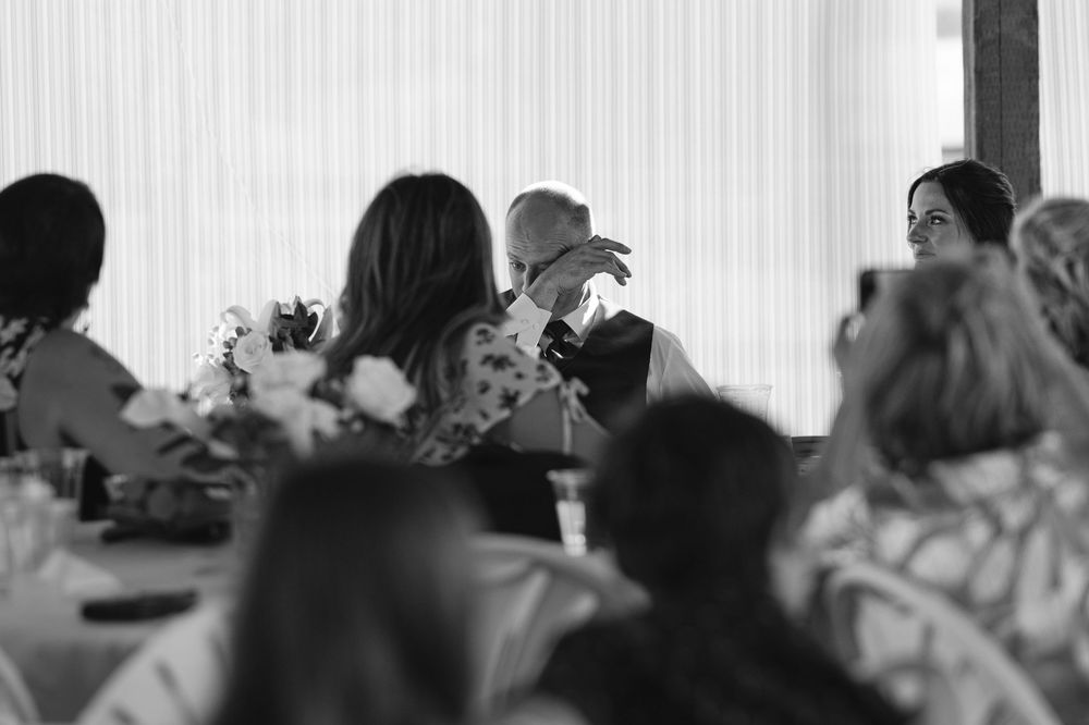 Black and white photo of wedding guests gathered around tables during a reception celebration.