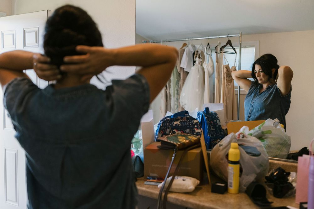 Person getting ready in front of a mirror with clothing rack visible in the background.