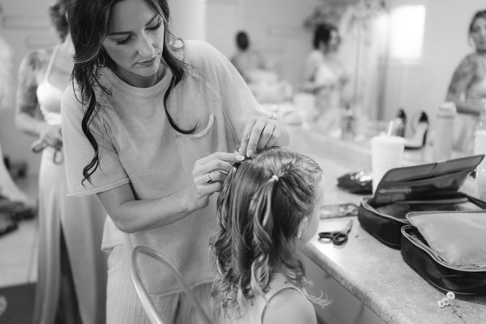 Wedding preparation scene with styling and makeup being done in a bright indoor setting.