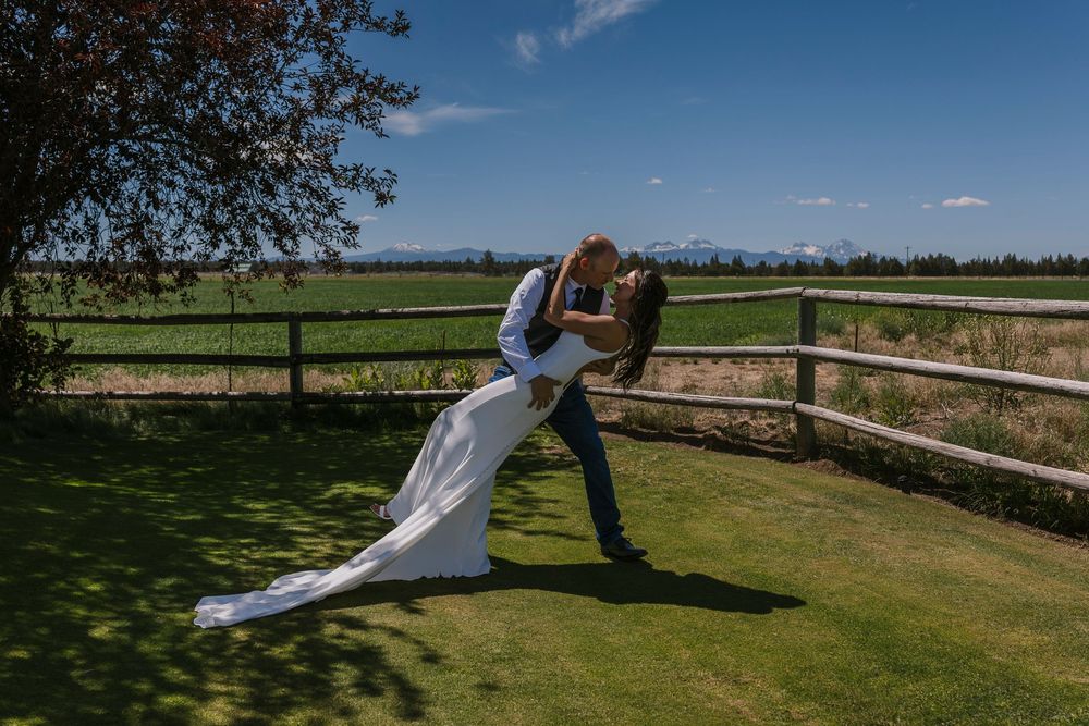 A couple shares a playful moment along a rustic wooden fence on a sunny day.