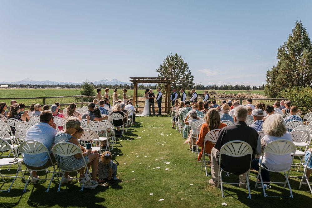 Guests seated in rows of chairs on a lawn watching an outdoor wedding ceremony with mountain views.