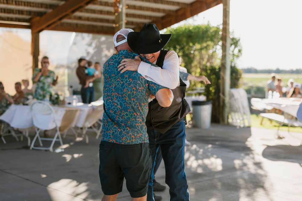 Guests embrace and celebrate during an outdoor gathering under a covered patio.