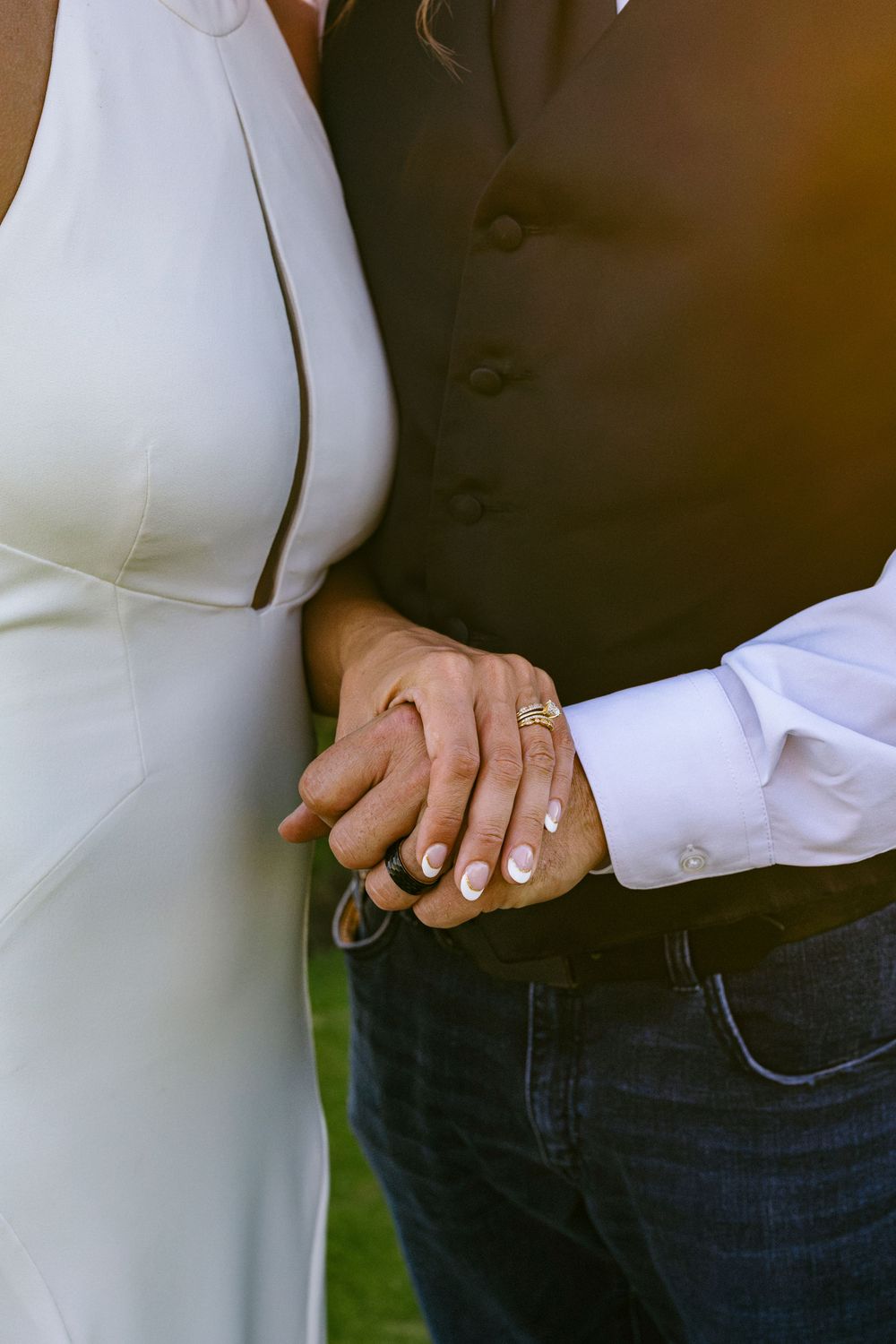 Close-up view of joined hands showing wedding rings and white dress details against a dark suit.
