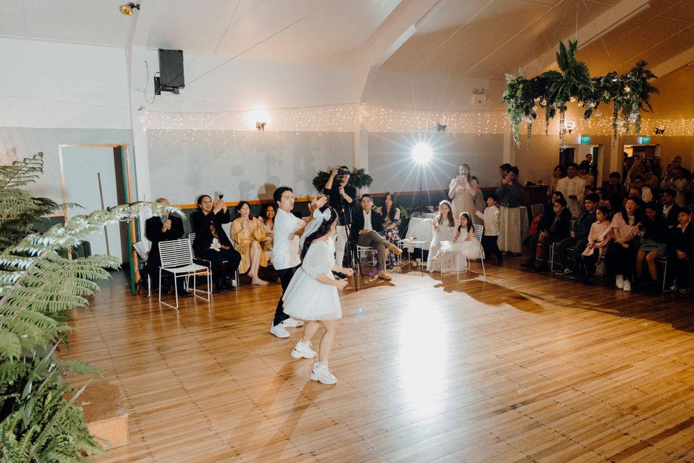 Dancers performing at a wedding reception in a bright indoor venue with wooden floors and decorative greenery.