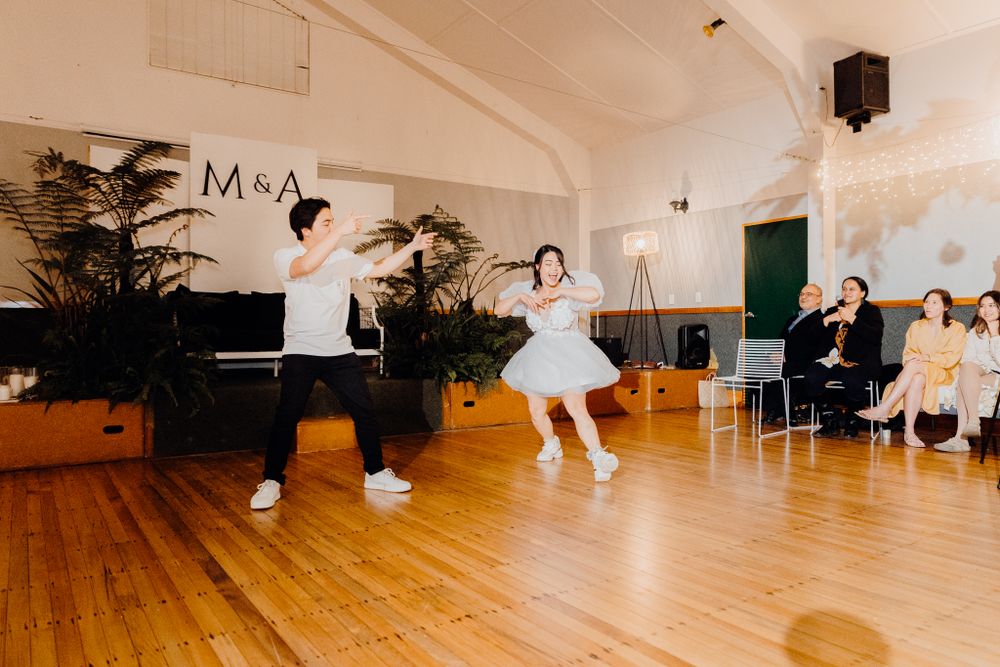 High-energy dance performance in front of seated guests with M&A signage and tropical plants decorating the space.