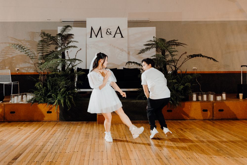Energetic dance moves being showcased on a polished wooden floor with decorative greenery and M&A branding.