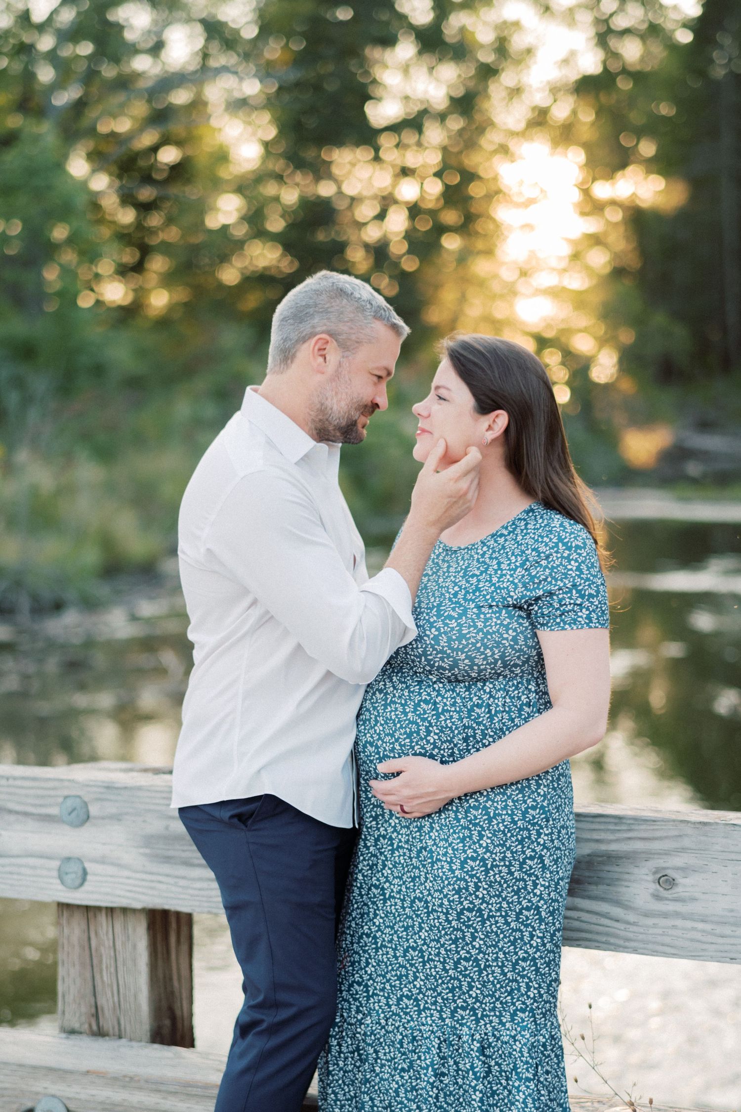 Intimate maternity photo of couple embracing by a pond at golden hour.