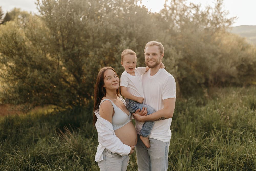 A family maternity photo outdoors with a small child in a natural setting.