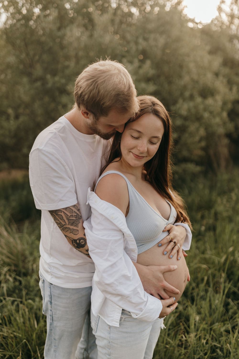 A tender maternity moment captured at sunset in a natural outdoor setting.