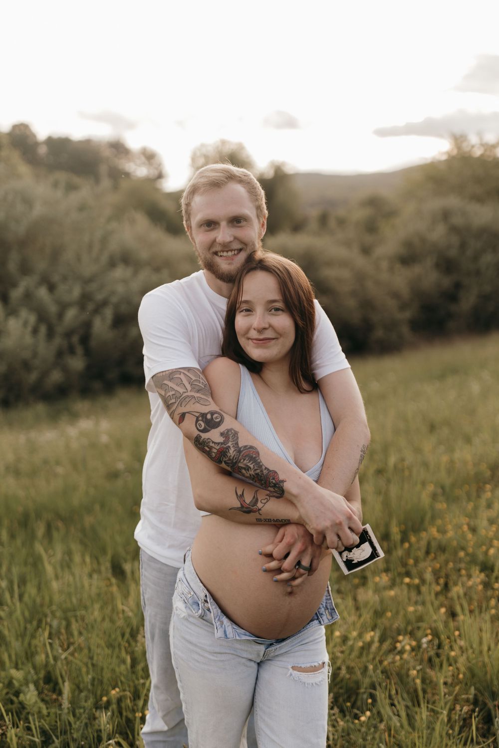 A loving maternity portrait captured in golden hour light with natural outdoor scenery.