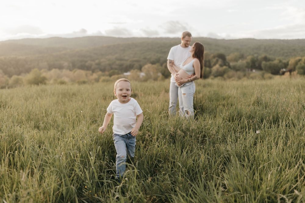 A candid family moment in a meadow with a child running through tall grass.