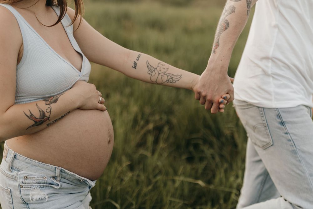 A close-up shot of tattooed hands holding each other with a pregnant belly in view.