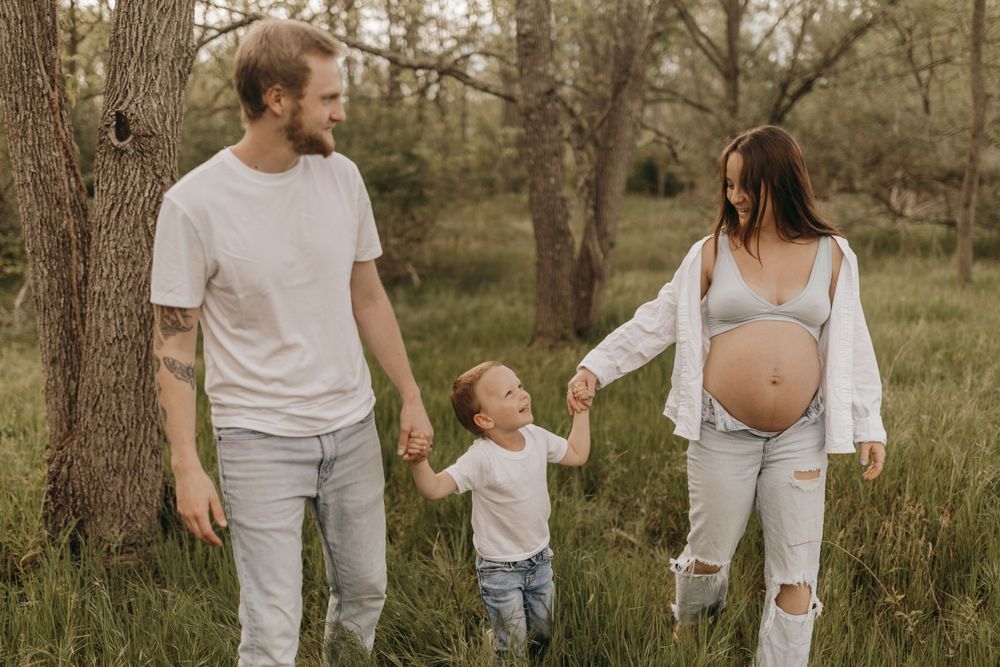 Family holding hands while walking through a grassy field with trees.