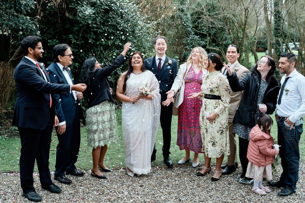Guests celebrate by throwing flower petals at a joyful outdoor wedding ceremony.