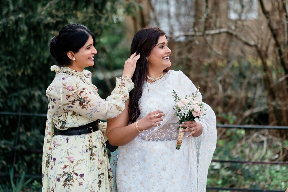 Two figures wearing lace white dresses stand together in an outdoor garden setting.