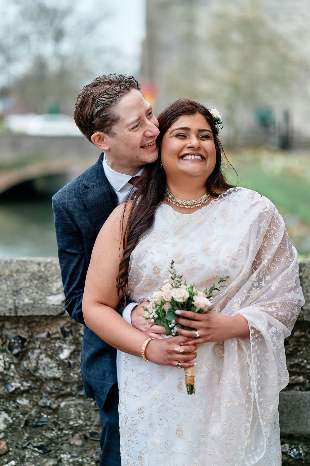 A joyful couple shares a romantic moment at their wedding, with the bride wearing a white sari and holding a bouquet.