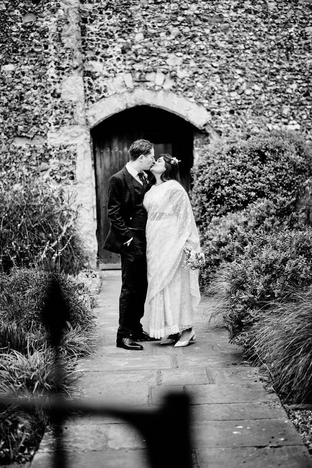 A romantic black and white photo sequence shows a couple sharing an umbrella kiss in a garden walkway.
