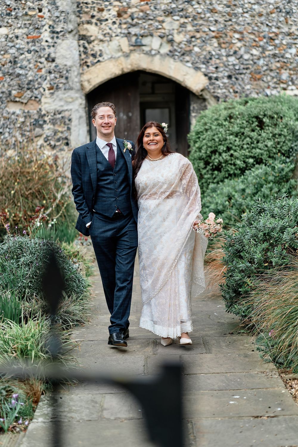 Formal couple photographed against stone wall and garden foliage in sequence of walking shots.