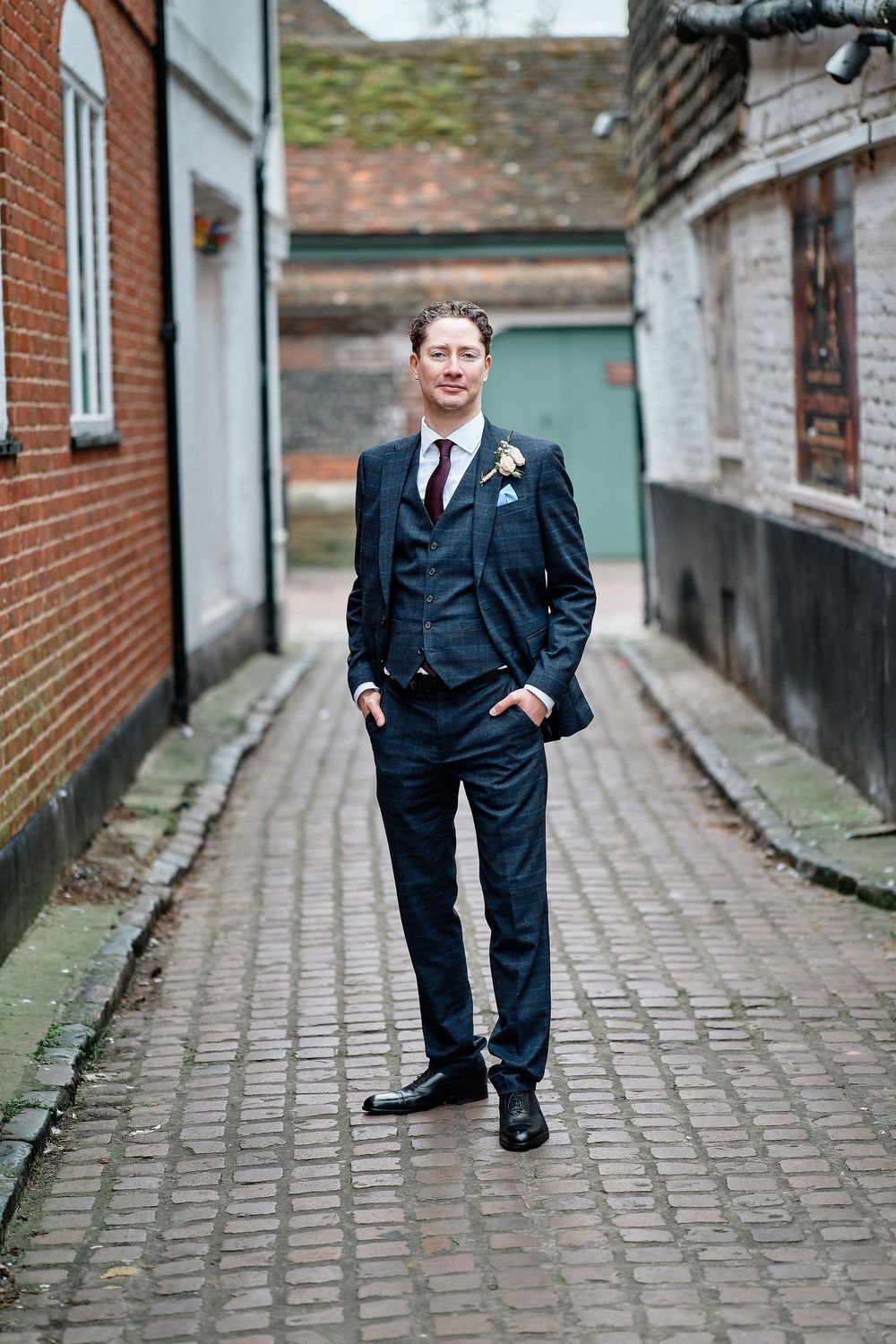 A young ring bearer in a navy suit poses along a brick-lined alleyway during a wedding ceremony.