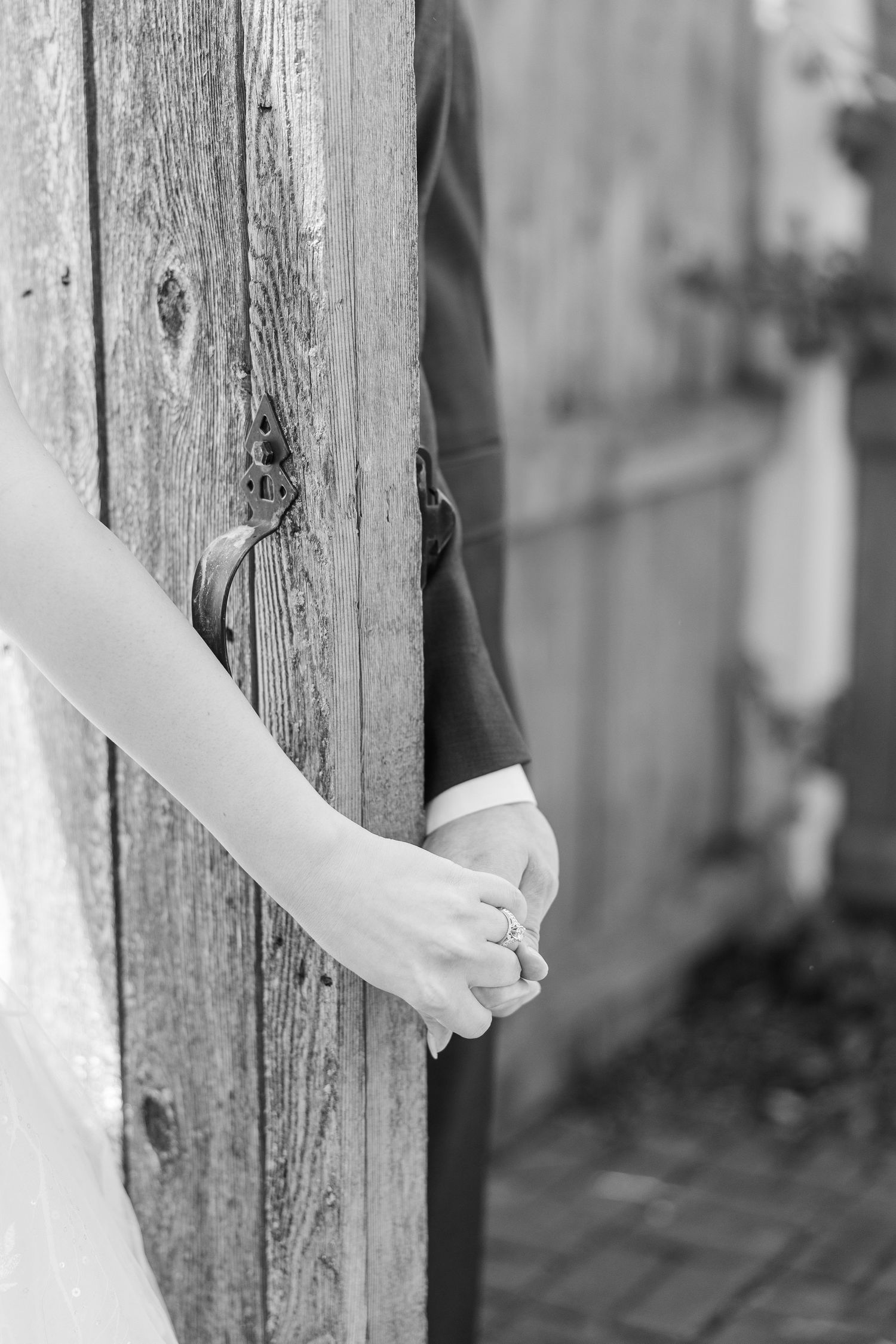 Two hands meeting around a rustic wooden fence post in a tender moment during what appears to be a wedding.
