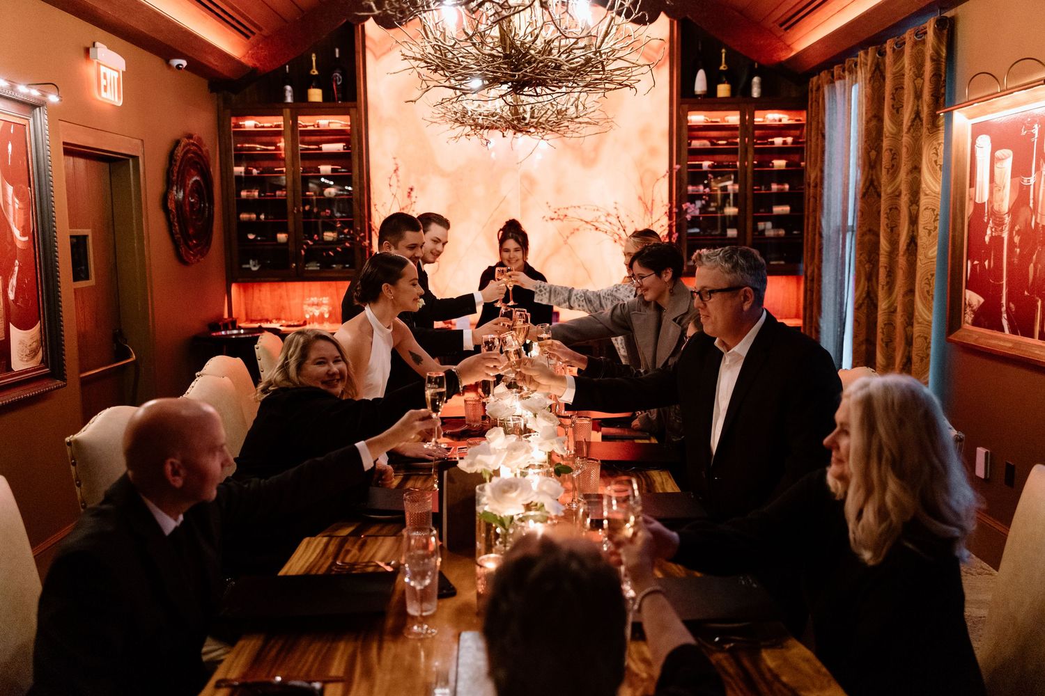 People gather in a dimly lit restaurant with warm lighting and elegant chandeliers during an evening event.