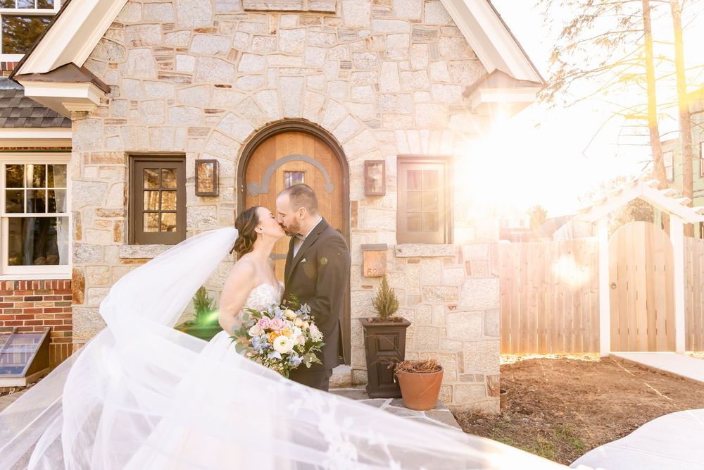 A romantic sunset wedding portrait outside a charming stone cottage with a glowing backlit veil.
