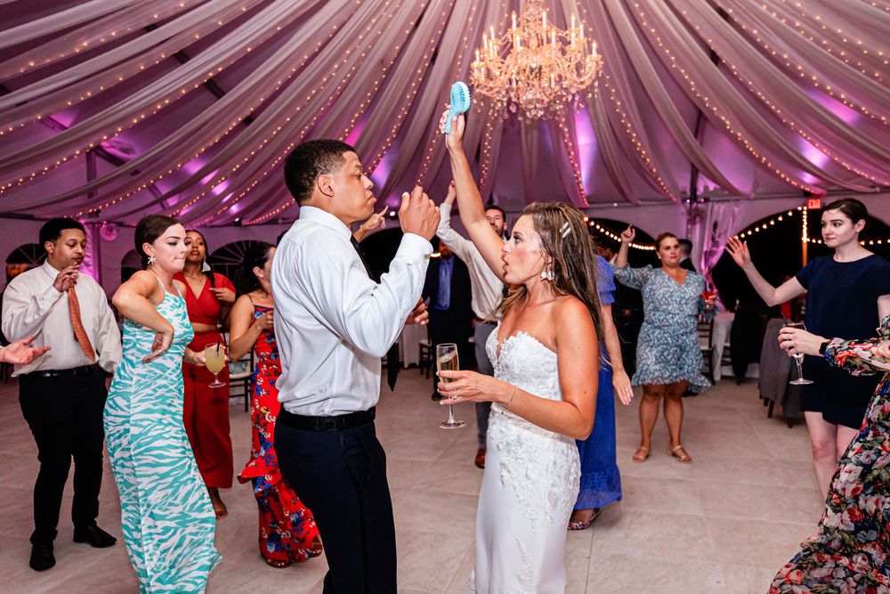 Wedding reception guests dance under draped fabric ceiling with crystal chandelier in pink and purple lighting.