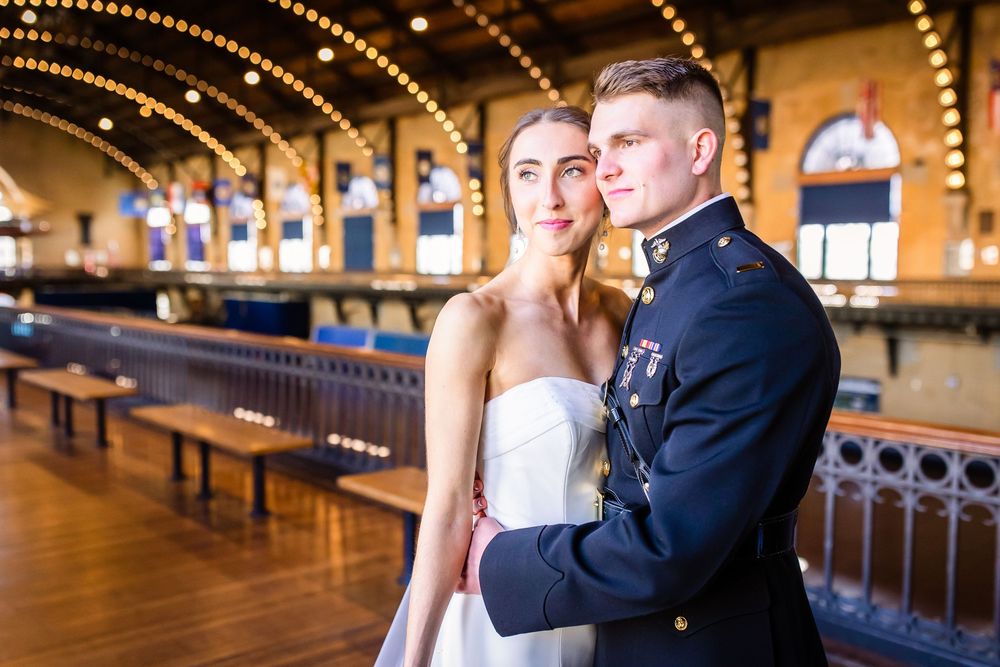 A couple stands together in a historic ballroom with wooden floors and ornate details illuminated by warm lighting.