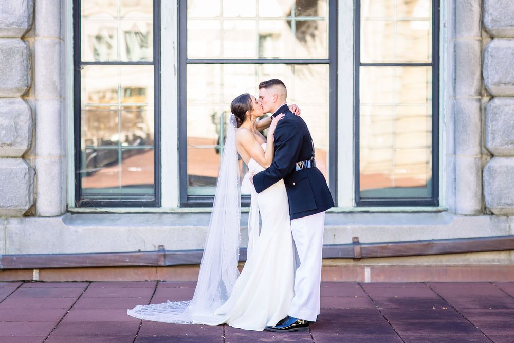 A romantic wedding couple shares a tender moment in front of large stone windows on their special day.