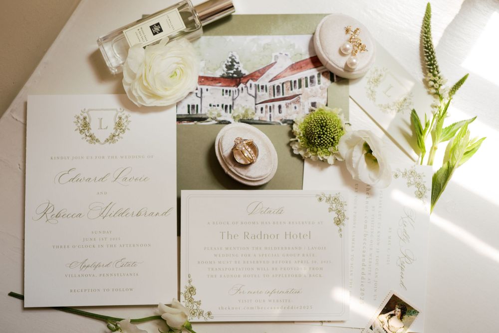 Elegant wedding invitation suite with green and white florals displayed alongside perfume and decorative items in natural light.