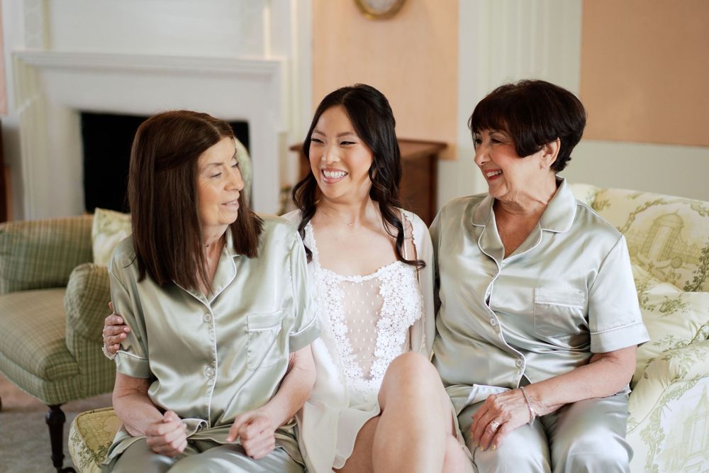 Three people in matching satin sleepwear share a joyful moment while sitting together on a beige couch.