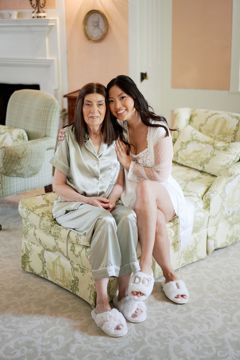Two people sitting together on a floral couch wearing matching fuzzy slippers in an elegant living room.