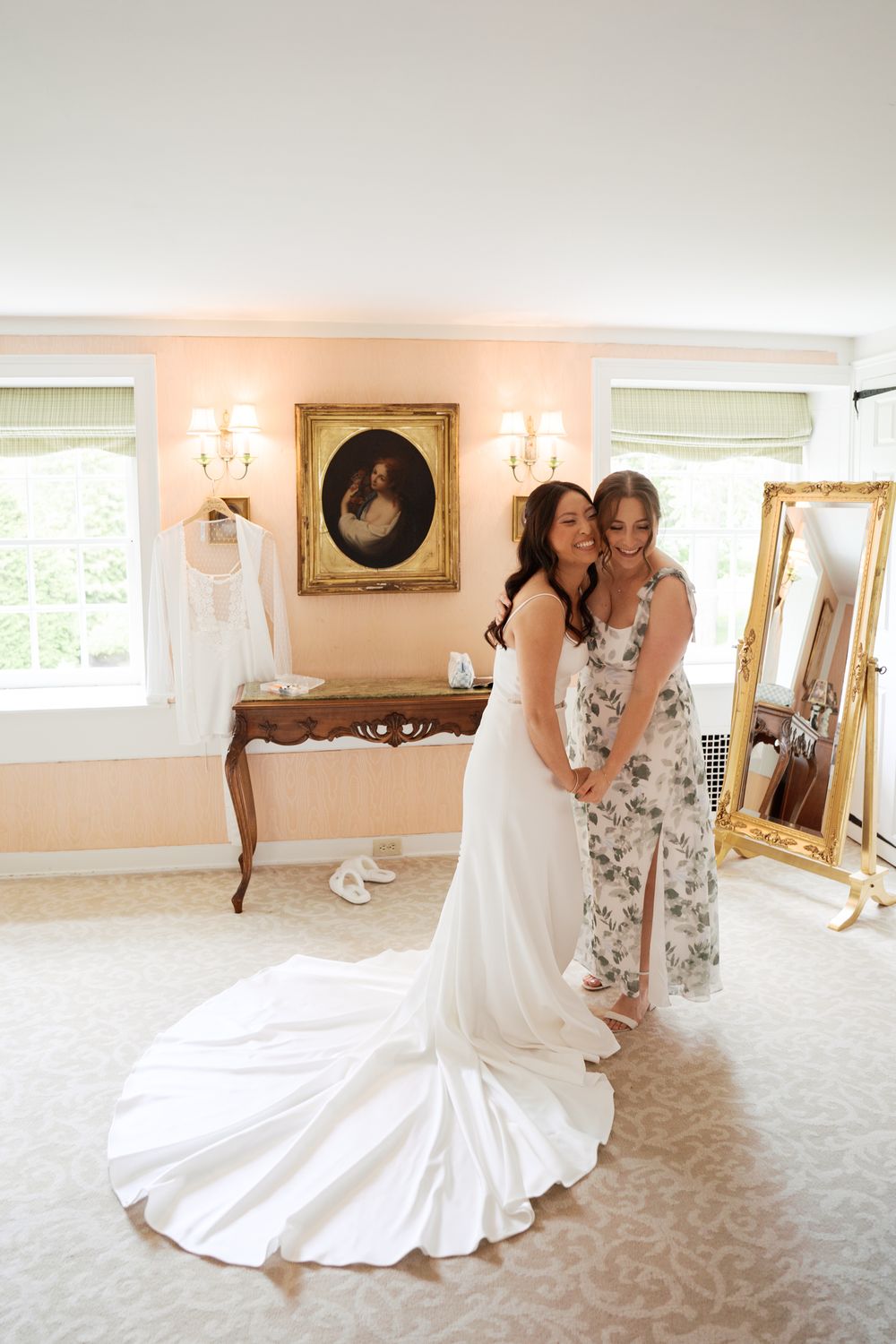 A white wedding dress with dramatic train photographed in an elegant dressing room with gold-framed mirrors and sconces.