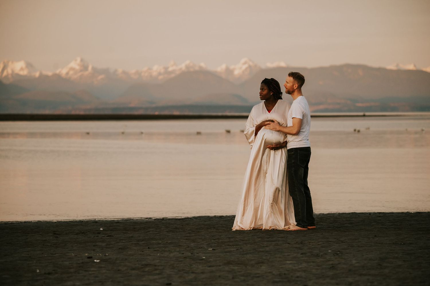 Maternity portrait photography of couple holding bump at kye bay beach by ocean and mountains Comox Valley Vancouver Island photographer