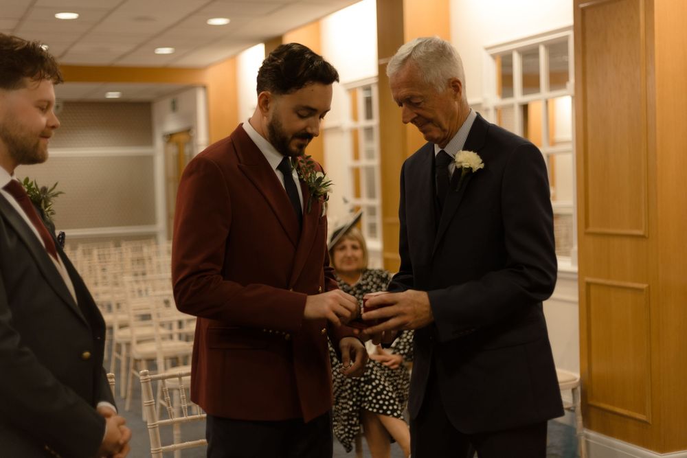 Two people in formal attire interact at an indoor event venue with wooden doors and hallway lighting.